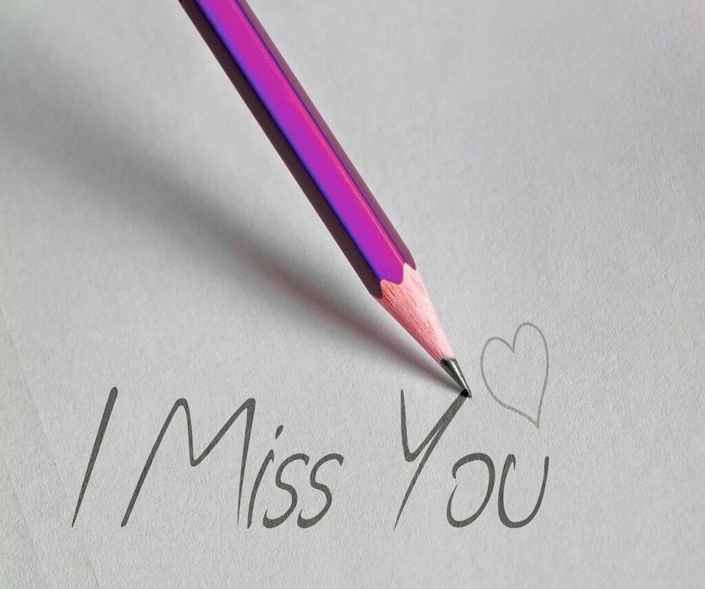 ein rosa Bleistift der die Wörter "I Miss You" sowie ein Herz auf ein Blatt schreibt